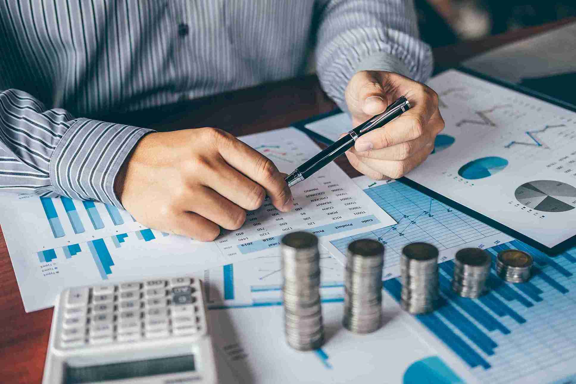 An accountant is analysing financial data and coin stacks on desk.