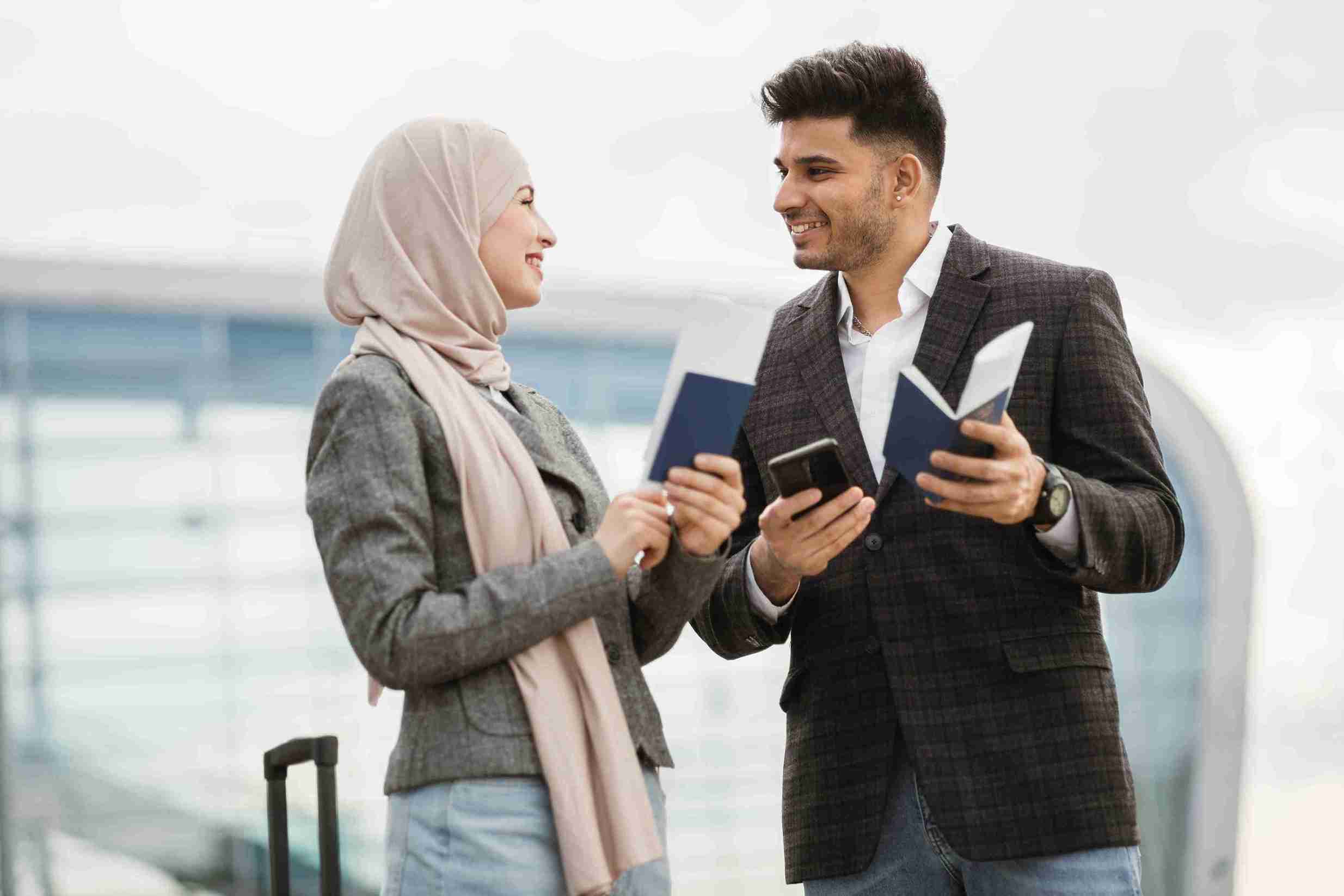 Couple standing outside airport terminal with passport in hand.
