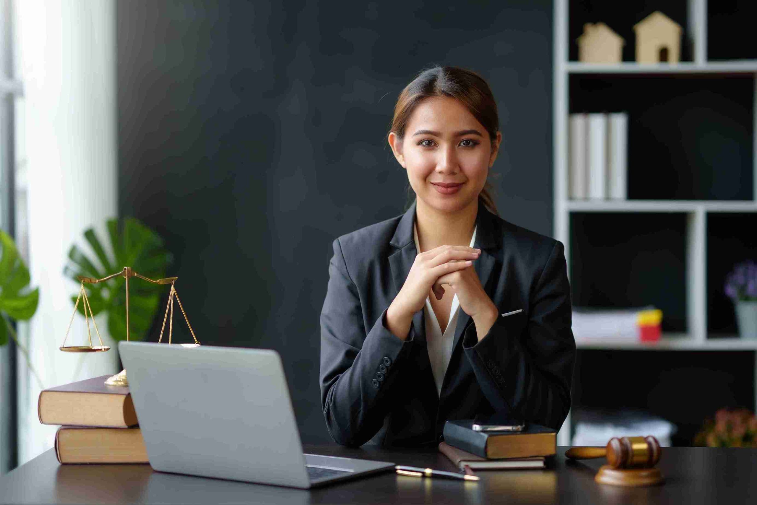 A women in suit at desk with laptop.